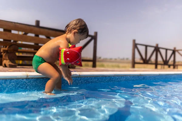 Chlapec s náramky hrající si s hračkami u bazénu s průzračnou vodou na pozadí letního západu slunce — Stock fotografie