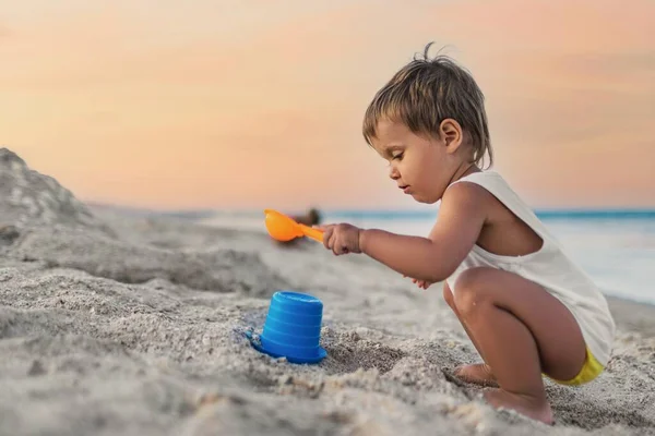 Ragazzo che gioca con i giocattoli sulla spiaggia costruendo perline e torrette sorridenti a qualcuno dietro le quinte durante le vacanze estive — Foto Stock