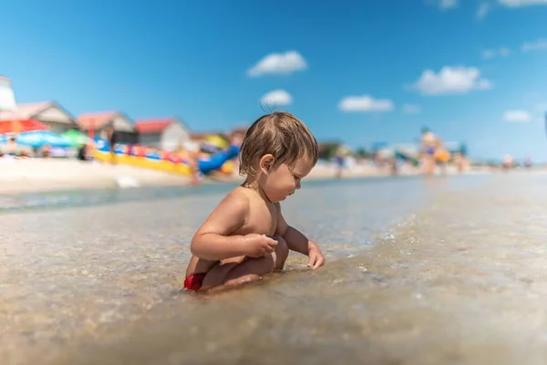 Niño recoge conchas y guijarros en el mar en un fondo arenoso bajo el sol de verano en unas vacaciones — Foto de Stock