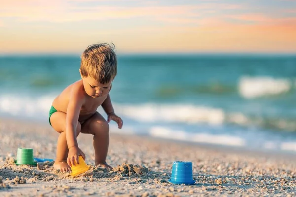 Ragazzo che gioca con i giocattoli sulla spiaggia costruendo perline e torrette sorridenti a qualcuno dietro le quinte durante le vacanze estive — Foto Stock