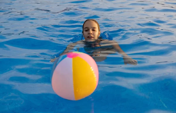 Una chica en un traje de baño brillante nada con una pelota inflable en una piscina con agua clara en una noche de verano — Foto de Stock