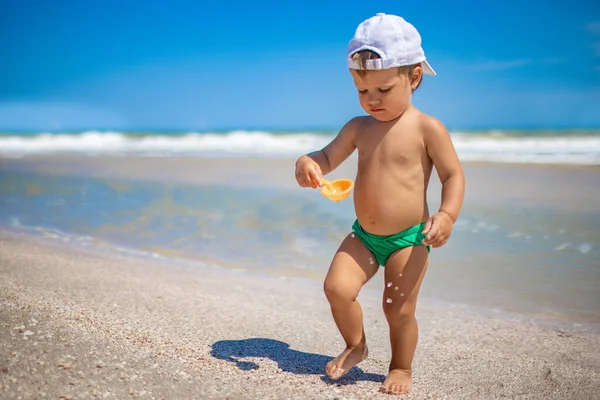 Ragazzo raccoglie conchiglie e ciottoli in mare su un fondo sabbioso sotto il sole estivo in vacanza — Foto Stock