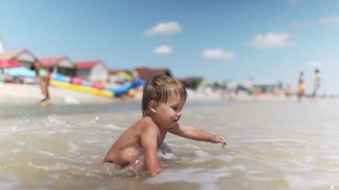 Çocuk yaz güneşinin altında kumlu bir zeminde deniz kabukları ve çakıl taşları topluyor.