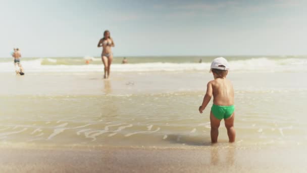 Niño recoge conchas y guijarros en el mar en un fondo arenoso bajo el sol de verano en unas vacaciones — Vídeo de stock