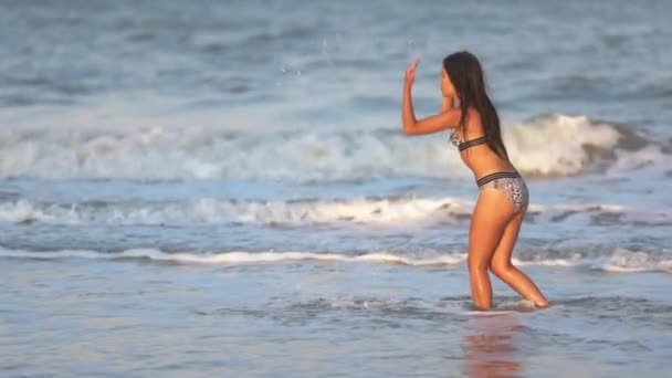 Una chica con el pelo suelto camina sobre el mar con olas y disfruta del sol — Vídeo de stock