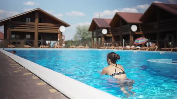 Fille en maillot de bain léopard nage dans une piscine avec de l'eau bleue un jour d'été — Video