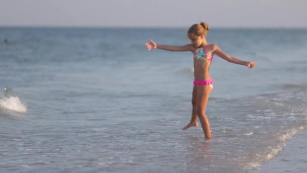 Menina brincando com ondas chutando e girando sob o sol de verão desfrutando as férias — Vídeo de Stock
