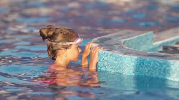 Ein Mädchen im hellen Badeanzug mit Schwimmbrille taucht in einen Pool mit klarem, transparentem Wasser — Stockvideo