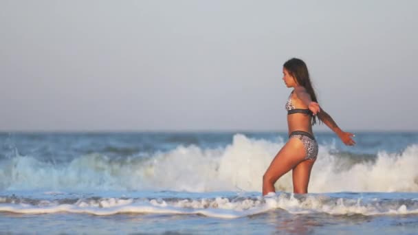 Una chica con el pelo suelto camina sobre el mar con olas y disfruta del sol — Vídeo de stock