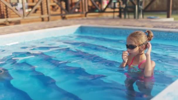 Девушка в ярком купальнике в купальных очках ныряет в бассейн с прозрачной водой — стоковое видео