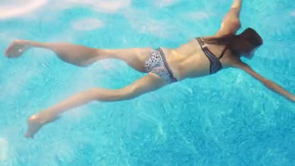 Flicka i leopardbaddräkt badar på magen under vattnet i en pool med klart vatten på sommarlovet — Stockvideo