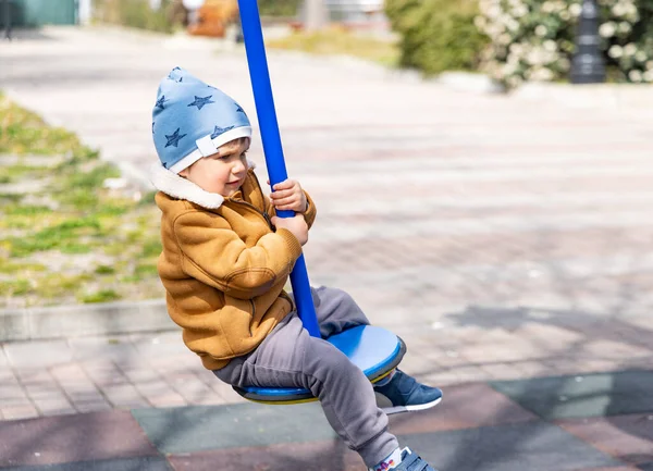 Хлопчик на дитячому майданчику в осінньому парку їде на гойдалці в похмуру погоду — стокове фото