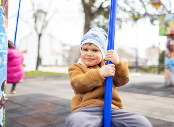 Хлопчик на дитячому майданчику в осінньому парку їде на гойдалці в похмуру погоду — стокове фото