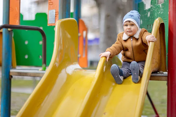 Хлопчик грає на ігровому майданчику і катається на слайді в осінню погоду — стокове фото