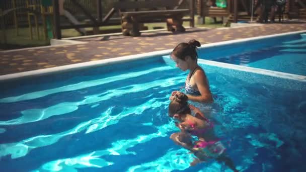 Elder sister in leopard swimsuit pulls little sister out of the pool with blue water — Wideo stockowe
