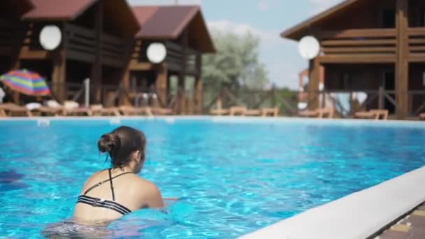 Girl in a leopard swimsuit swims in a pool with blue water on a summer day — Αρχείο Βίντεο