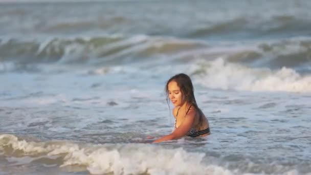 Ragazza con i capelli bagnati in un costume da bagno leopardato spruzza acqua mentre seduto in mare — Video Stock