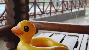 Şişme bir ördek, çardaktaki ahşap masanın üzerinde dinlenme merkezinde, yağmurla kaplı bir havuzun zeminine uzanır.