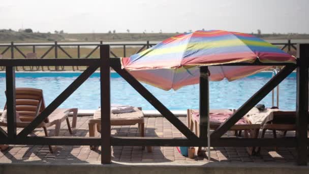 Tempo de verão no resort, os raios de sóis brilham nas espreguiçadeiras com guarda-sóis na piscina do hotel — Vídeo de Stock