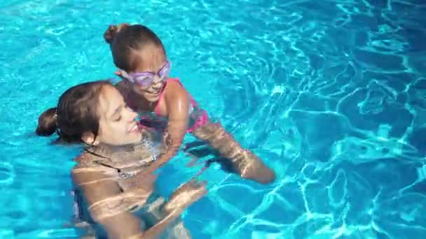 Dos chicas en bikinis brillantes están jugando juntas en una piscina con agua azul en un día de verano en unas vacaciones tan esperadas — Vídeo de stock