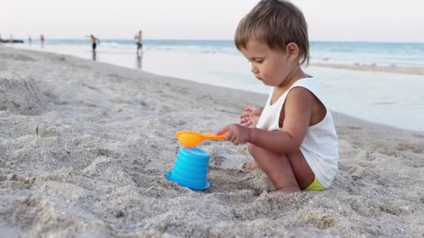 Хлопчик грає з іграшками на пляжі будівельні намистини і башти посміхаються комусь за лаштунками на літніх канікулах — стокове відео