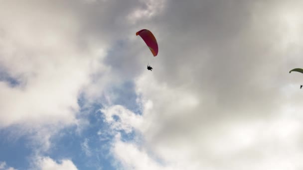 As pessoas tentam parapente voando com paraquedas contra nuvens — Vídeo de Stock
