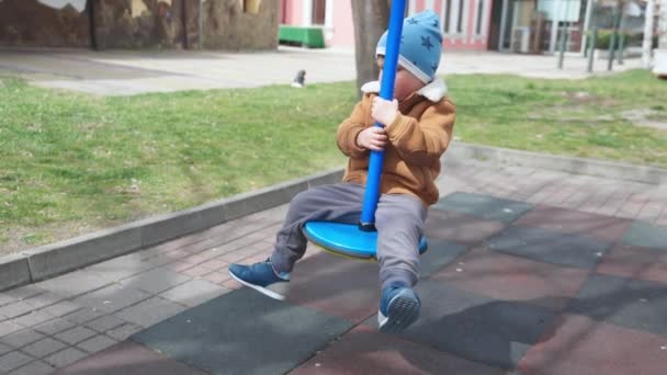 A boy on a playground in an autumn park rides on a swing in cloudy weather — Stockvideo