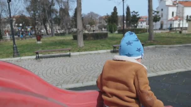 The boy plays on the playground and rides a slide in autumn weather — Vídeo de Stock