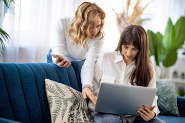 Tişörtlü iki kız telefona ve dairede bir dergiye bakarken bir şey tartışıyorlar.