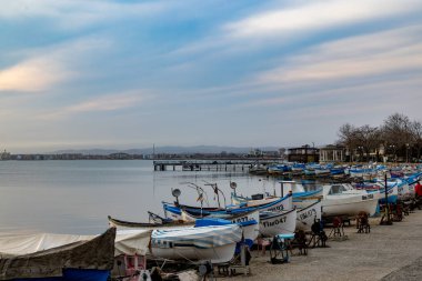 Birçok küçük eski beyaz tekne ve kayıklar bir taş üzerinde ve beton geniş rıhtım sakin mavi sakin Karadeniz yakınında, parlak, güneşli bir günbatımı ve bulutlu bir gökyüzü karşı