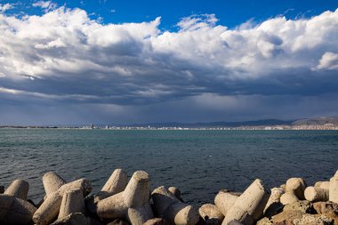 Geniş mavi bulutlu gökyüzünün arka planına karşı küçük, güvenilir bir dalgakıran ve beyaz deniz güçlü dalgaları ile öfkeli, mavi bir Karadeniz.
