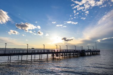 Sakin, sakin bir Karadeniz 'de, bulutlu, çok renkli bir gökyüzü ve parlak bir akşam günbatımına bakan eski, boş, küçük bir iskelenin yan görüntüsü.