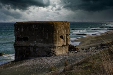 İkinci Dünya Savaşı 'ndan beri sakin, yeşil, sessiz Karadeniz' in yakınındaki kumlu ve vahşi bir kumsalda terk edilmiş küçük beton bir sığınak güçlü renkli bulutlu bir gökyüzünün zeminine karşı duruyor.