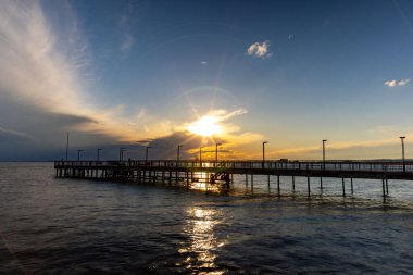 Sakin, sakin bir Karadeniz 'de, bulutlu, çok renkli bir gökyüzü ve parlak bir akşam günbatımına bakan eski, boş, küçük bir iskelenin yan görüntüsü.