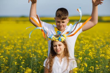 Önemseyen ağabeyi, parlak Ukrayna çiçek çelenkleriyle çok renkli ince kurdeleler örüyor. Küçük, gülümseyen kız kardeşin başında. Açık mavi gökyüzünün altında bitmeyen kolza tohumu tarlasında.