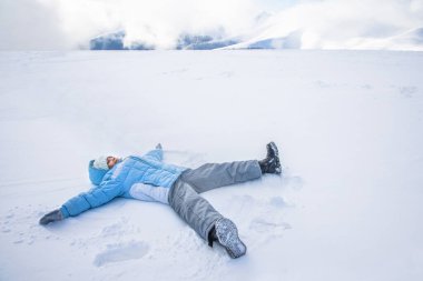 Taze, derin karda kar meleği yapan küçük tatlı bir kızın manzarasının üstünde. Kayak kıyafetleri giyen, yalan söyleyen, kollarını ve bacaklarını sallayan, parkta melek yapan bir kadın çocuk. Kış aktiviteleri kavramı.