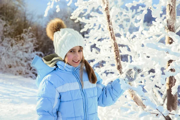 Güneşli bir günde dağlarda ağaçların karlı dallarını sallayan eldivenli güzel bir kızın yan görüntüsü. Neşeli bayan çocuk gülümsüyor, arka planda buzlu ağaçlarla karların tadını çıkarıyor. Kış tatili kavramı.