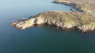 Bulgaristan 'ın parlak güneşli akşam günbatımına karşı sakin, mavi yansıtıcı Karadeniz ve eski karanlık kayalık taşlarla kaplı deniz manzarası. UHD 4K video gerçek zamanlı