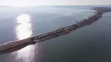 Kuşlar, Bulgaristan 'da açık mavi gökyüzü altında dalgalanan derin turkuaz Karadeniz' le çevrili kuru yabani çimenler ve küçük eski evlerle dar kumlu ve kayalık sahile bakıyor. UHD 4K video gerçek zamanlı