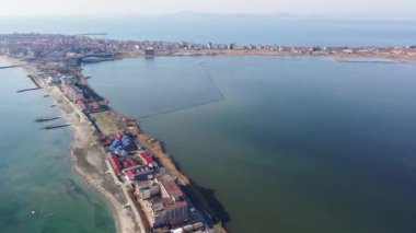 Kuşlar, Bulgaristan 'da açık mavi gökyüzü altında dalgalanan derin turkuaz Karadeniz' le çevrili kuru yabani çimenler ve küçük eski evlerle dar kumlu ve kayalık sahile bakıyor. UHD 4K video gerçek zamanlı