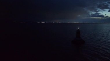 Bulgaristan 'ın hareketsiz Pomorie kasabası yakınlarında, derin ve sakin Karadeniz' de, gece bulutlu karanlık gökyüzünün altındaki eski bir deniz fenerinin kuş bakışı görüntüsü. UHD 4K video gerçek zamanlı