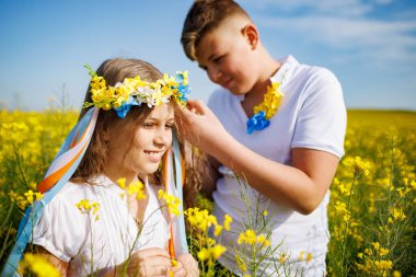 Önemseyen ağabeyi, parlak Ukrayna çiçek çelenkleriyle çok renkli ince kurdeleler örüyor. Küçük, gülümseyen kız kardeşin başında. Açık mavi gökyüzünün altında bitmeyen kolza tohumu tarlasında.