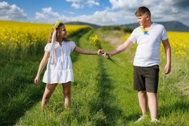 Küçük, parlak sarı bukete yakın, tarlada yabani küçük kolza tohumu çiçekleri bilinmeyen genç çocukların ellerinde, sonsuz tarlaların ve ılık yaz güneşi altında yeşil çayırların üzerinde