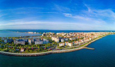 Bulgaristan 'ın Pomorie kentindeki antik tatil beldesi Pomorie' nin arka planına karşı derin ve sakin Karadeniz 'de yürüyen insanların bulunduğu deniz gezisi panoraması bulutlu, mavi bir gökyüzü altında