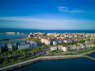 Bulgaristan 'ın Pomorie kentindeki antik tatil beldesi Pomorie' nin arka planında, bulutlu, mavi bir gökyüzü altında, derin ve sakin Karadeniz kıyısında yürüyen insanlarla deniz gezintisi.