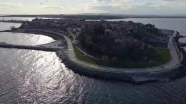 Bulgaristan 'ın Karadeniz kıyısındaki bir yarımadada yürüyen insanlarla dolu yeşil yay parkları ve dar caddelerle kaplı antik deniz kasabası Nesebar' a kuşların bakış açısı. UHD 4K video gerçek zamanlı