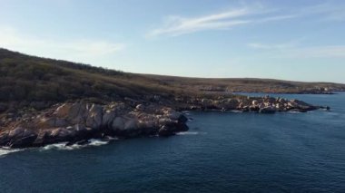 Bulgaristan 'ın parlak güneşli akşam günbatımına karşı sakin, mavi yansıtıcı Karadeniz ve eski karanlık kayalık taşlarla kaplı deniz manzarası. UHD 4K video gerçek zamanlı