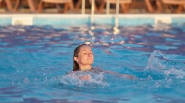 Güneşli, güneşli bir yaz günbatımında, ılık, sakin bir tatilde, berrak, şeffaf, serin bir suyla birlikte, koyu mavi bir havuzda yüzer. 4K UHD yavaş çekim videosu