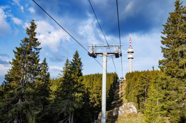 Güçlü ve güvenilir metal kablolu modern turist asansörü, Rodop Dağları 'nın dağ sıralarının arka planında, uzun tüylü, dikenli köknar ağaçlarıyla sonsuz yeşil ladin bahar ormanlarının arasından geçer.