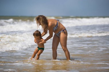 Neşeli, mutlu, şefkatli anne sıcak güneşin altında güneşli bir yaz tatilinde küçük komik oğlunu sakin mavi denizin üzerine fırlatıyor.